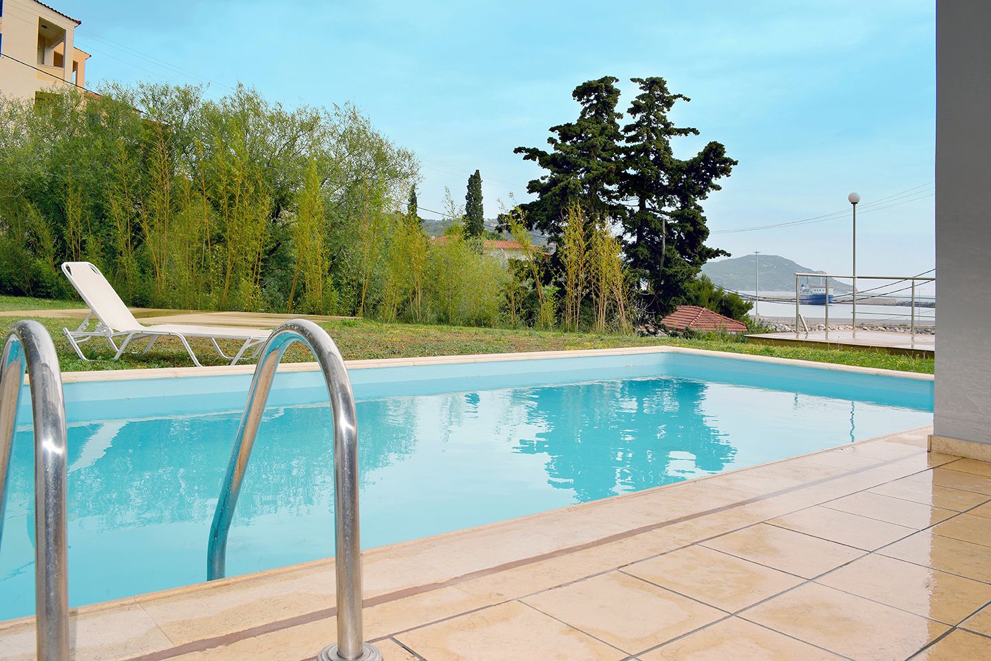 A swimming pool with a tiled deck, a metal ladder, and a white lounge chair.