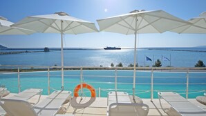 A poolside area with lounge chairs and umbrellas, overlooking a calm sea with a ship in the distance. - Kymi Palace Hotel (Kymi-Aliveri)