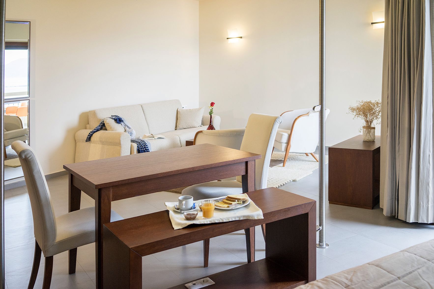 Une chambre d’hôtel moderne avec une table à manger en bois, un canapé et une petite table d’appoint sur laquelle est posé un vase.