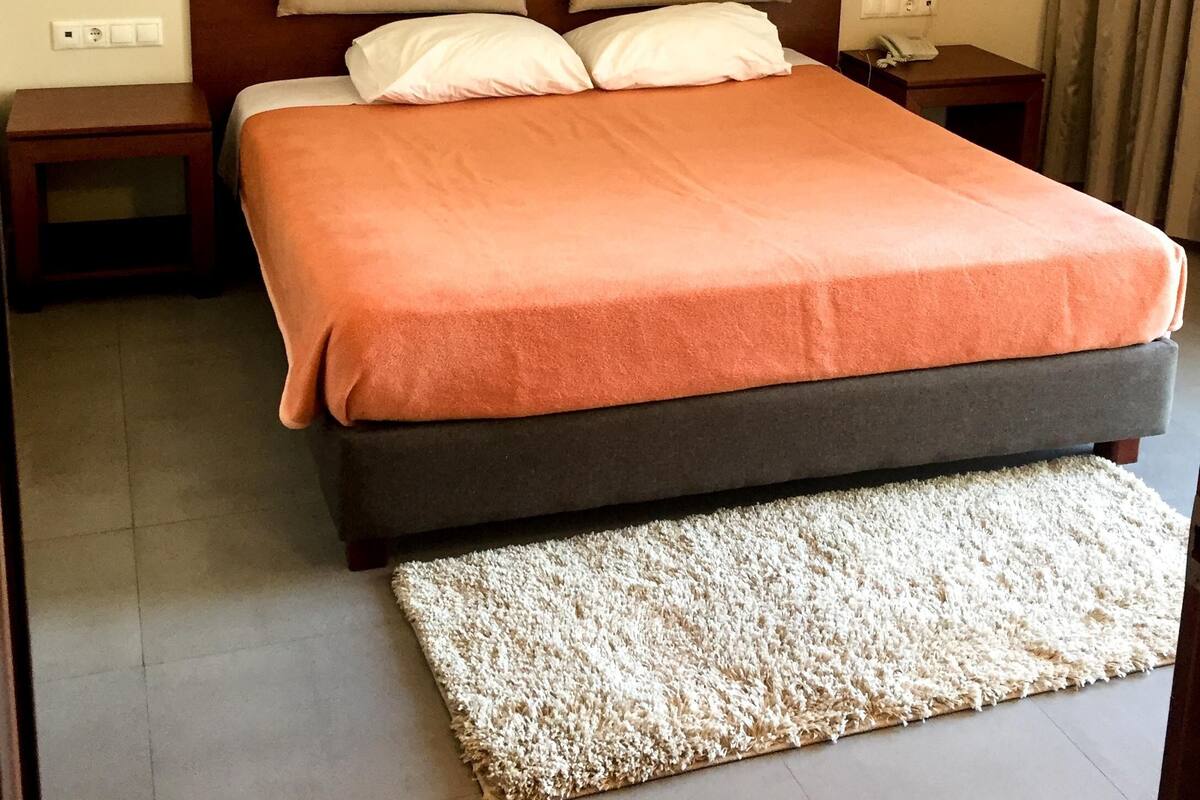 Una cama bien hecha con cabecera de madera, una mesita de noche pequeña y un teléfono en el tocador.