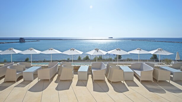 A terrace with white wicker furniture and umbrellas overlooking a calm sea. - Kymi Palace Hotel (Kymi-Aliveri)