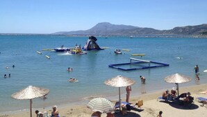 A beach with umbrellas, lounge chairs, and people swimming and sunbathing. - Kymi Palace Hotel (Kymi-Aliveri)