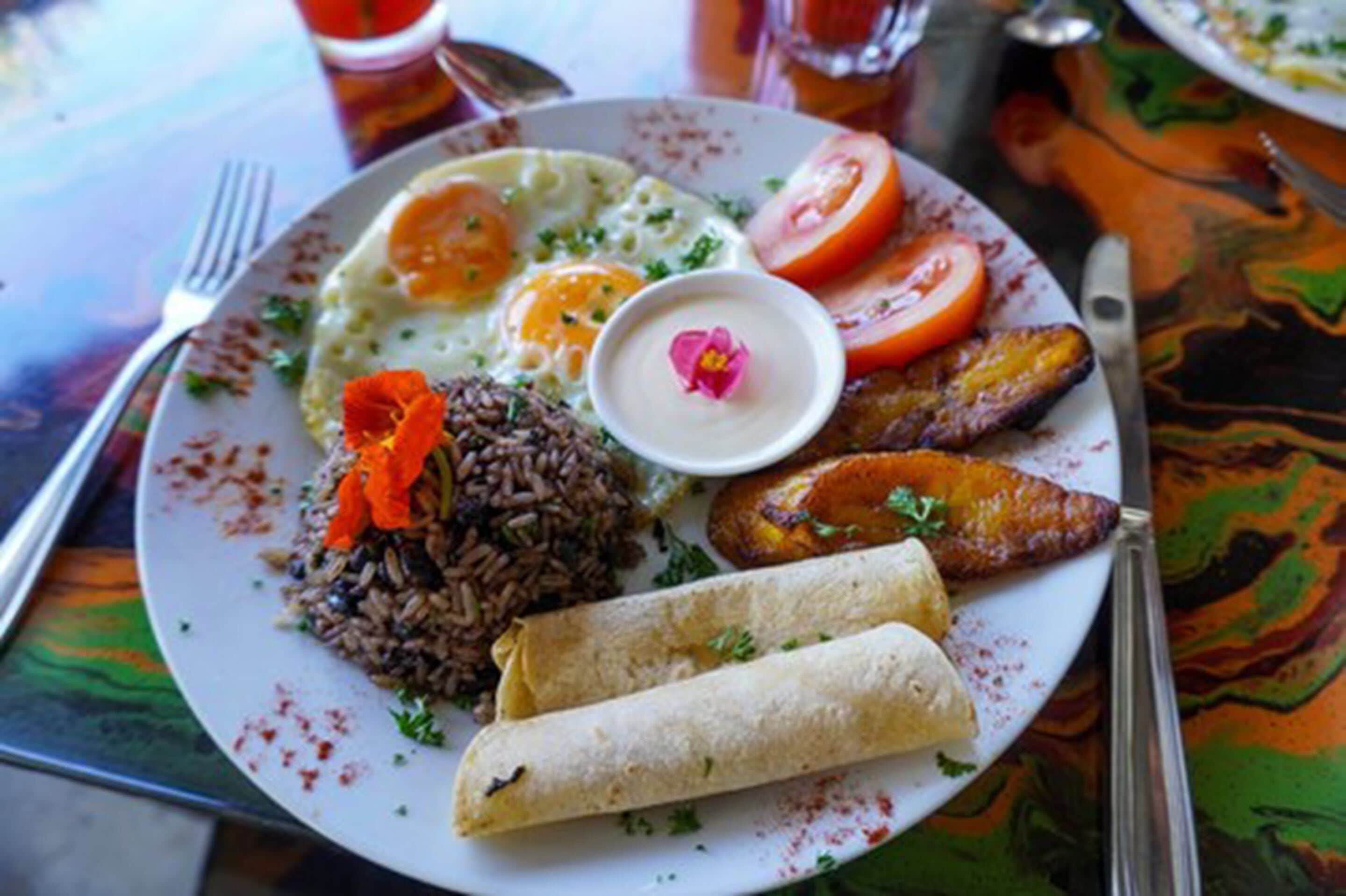 Ein Teller Essen mit gebratenen Eiern, schwarzem Reis, Kochbananen und einer kleinen Soßenportion.