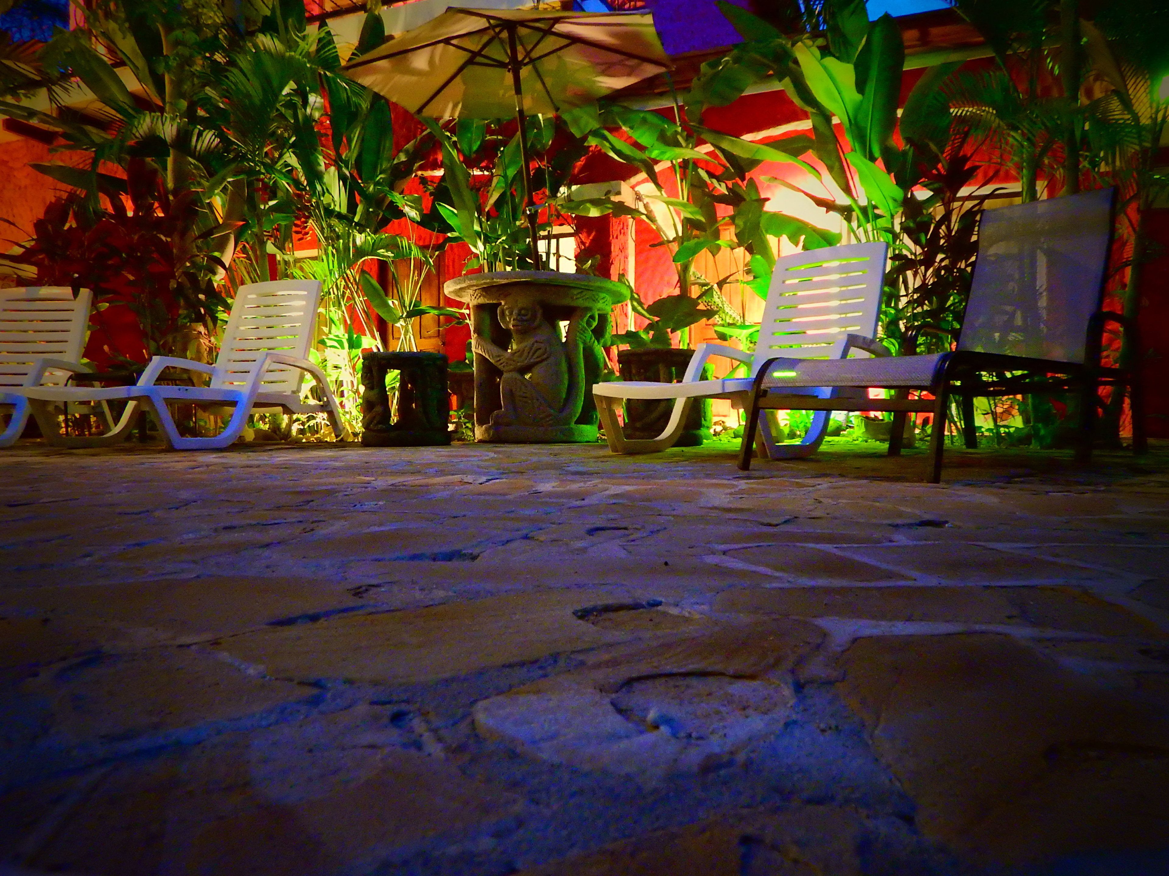 A patio area with stone flooring, white lounge chairs, and a variety of potted plants.