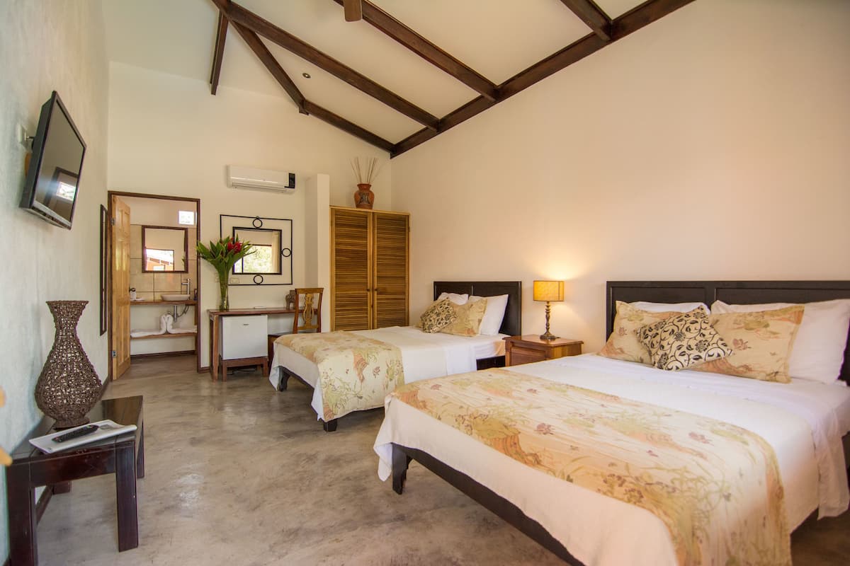 A hotel room with two beds, a desk with a chair, a TV, and a large mirror.