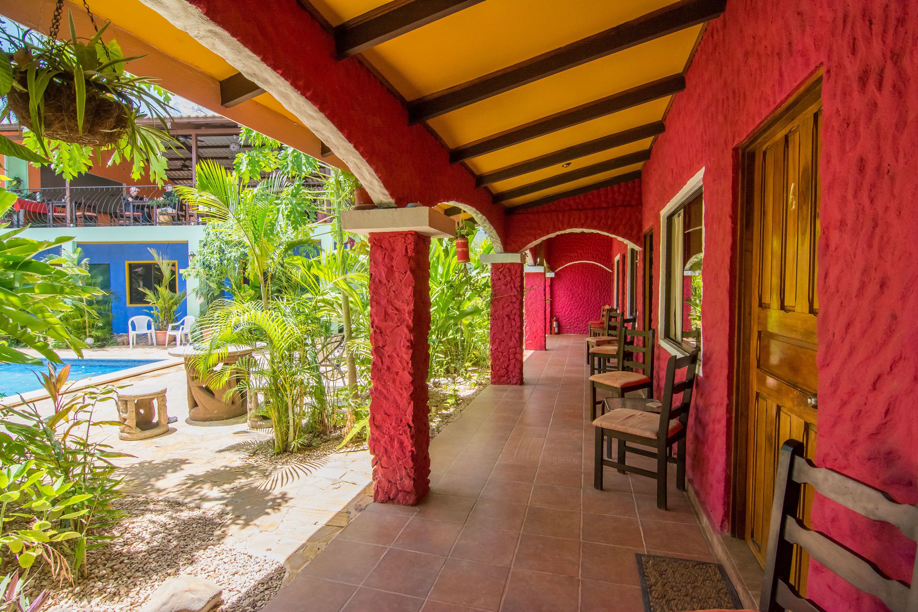 A covered outdoor area with a pool, red walls, and wooden furniture.