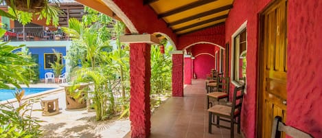 A covered outdoor area with a pool, red walls, and wooden furniture.