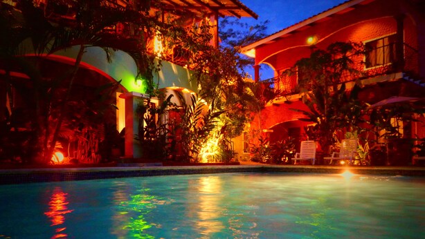 A swimming pool with reflections, surrounded by lush greenery and buildings with warm lighting. - Conchal Hotel (Cabo Velas)