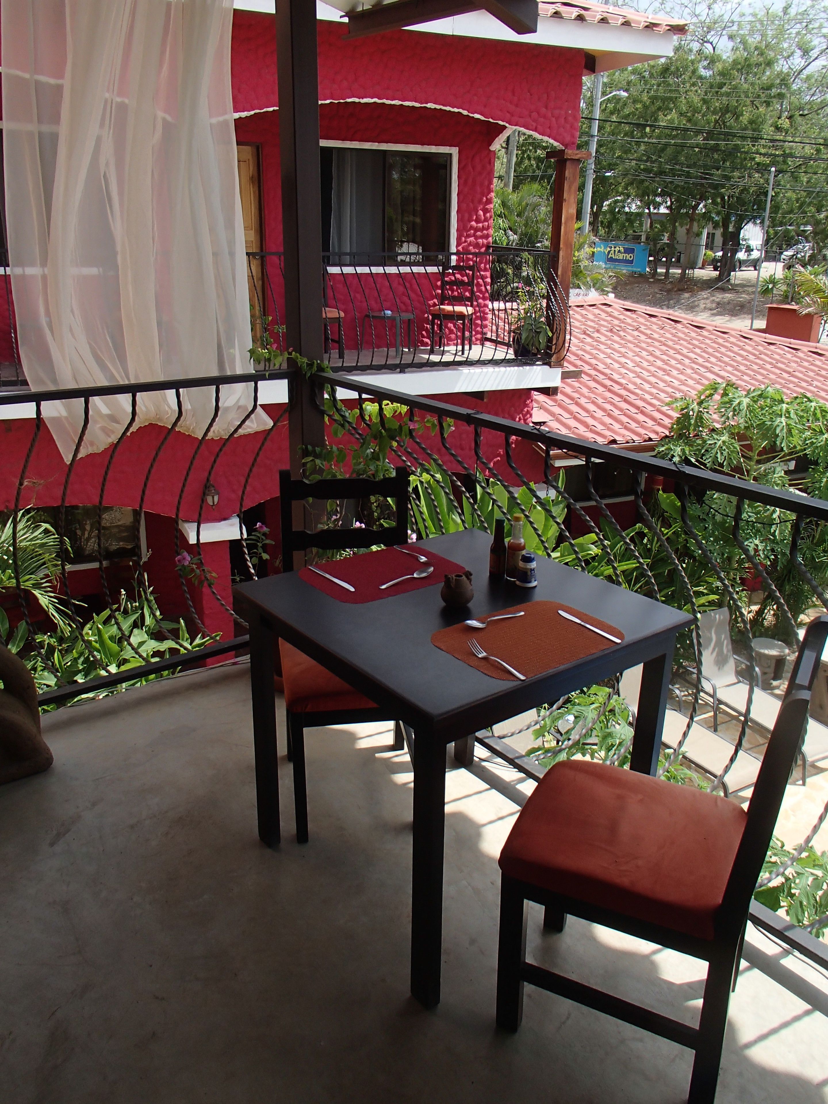 Varanda com mesa posta para dois, cadeiras e plantas em vasos.