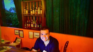 Una zona de bar con mostrador de madera, un atril para el menú y una estantería con botellas.