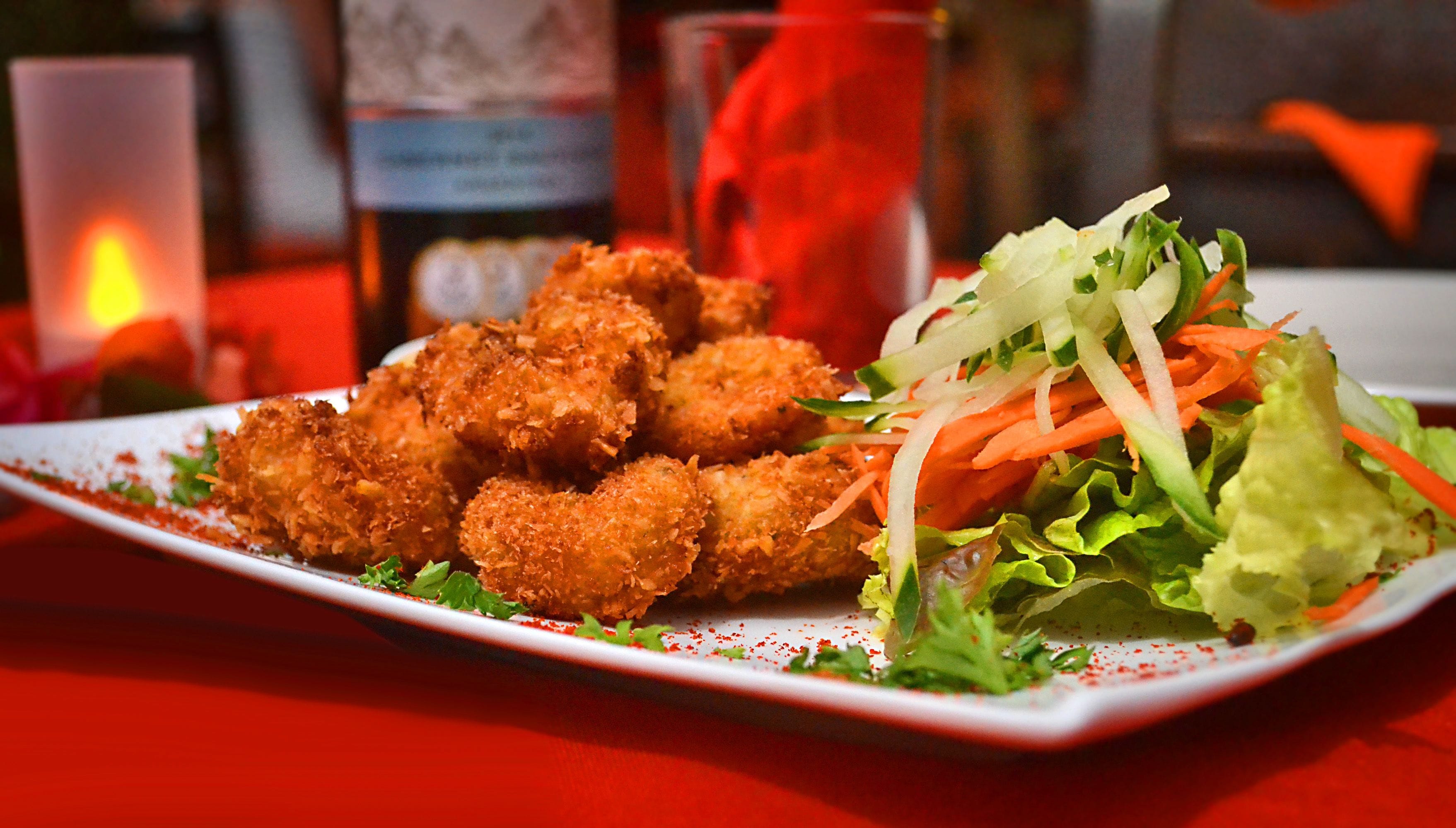 A plate of breaded and fried food items, possibly chicken nuggets, served with a side salad of lettuce, shredded carrots, and a creamy dressing.