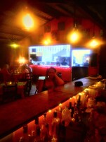 Zona de bar con mesas, botellas y mostrador.