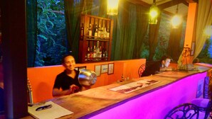 A bar area with a wooden counter, bar stools, and a view of trees through the window. - Conchal Hotel (Cabo Velas)