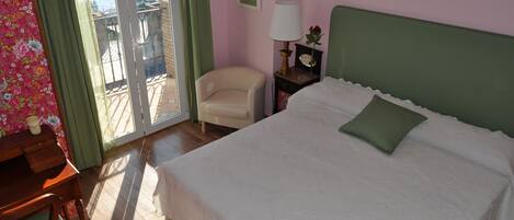 Une chambre à coucher comprenant un lit, une chaise, une table de chevet, une lampe et une vue sur l’extérieur, accessible par une porte coulissante.