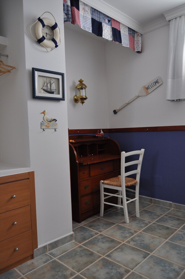 A room with a wooden dresser, a white chair, a framed picture of a ship, a life preserver, a welcome sign, and a wall-mounted lantern. - Welcome Inn Nerja (Nerja)