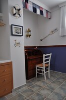 A room with a wooden dresser, a white chair, a framed picture of a ship, a life preserver, a welcome sign, and a wall-mounted lantern.