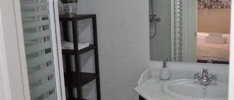 A bathroom with a white sink, dark wooden vanity, a glass shower enclosure, and a potted plant on a shelf.