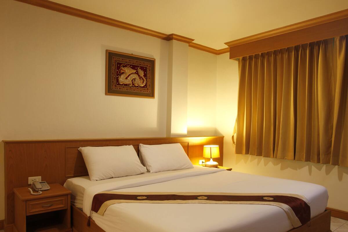 A hotel room with a large bed, wooden headboard, bedside table with a lamp, and a framed picture on the wall.