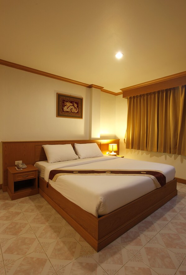 A hotel room with a large bed, wooden headboard, bedside table with a lamp, and a framed picture on the wall. - Casa Jip Guesthouse (Patong)