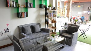 A living room with a grey sofa, two armchairs, a coffee table, and a bookshelf filled with books. - Casa Jip Guesthouse (Patong)