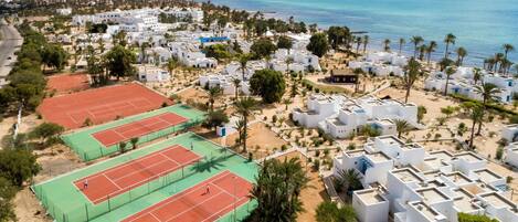 A coastal residential area with white buildings, a tennis court, and a beach in the background.