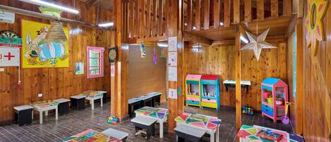 A room with wooden walls and ceiling, featuring tables with children's games, a colorful playhouse, and a star decoration.