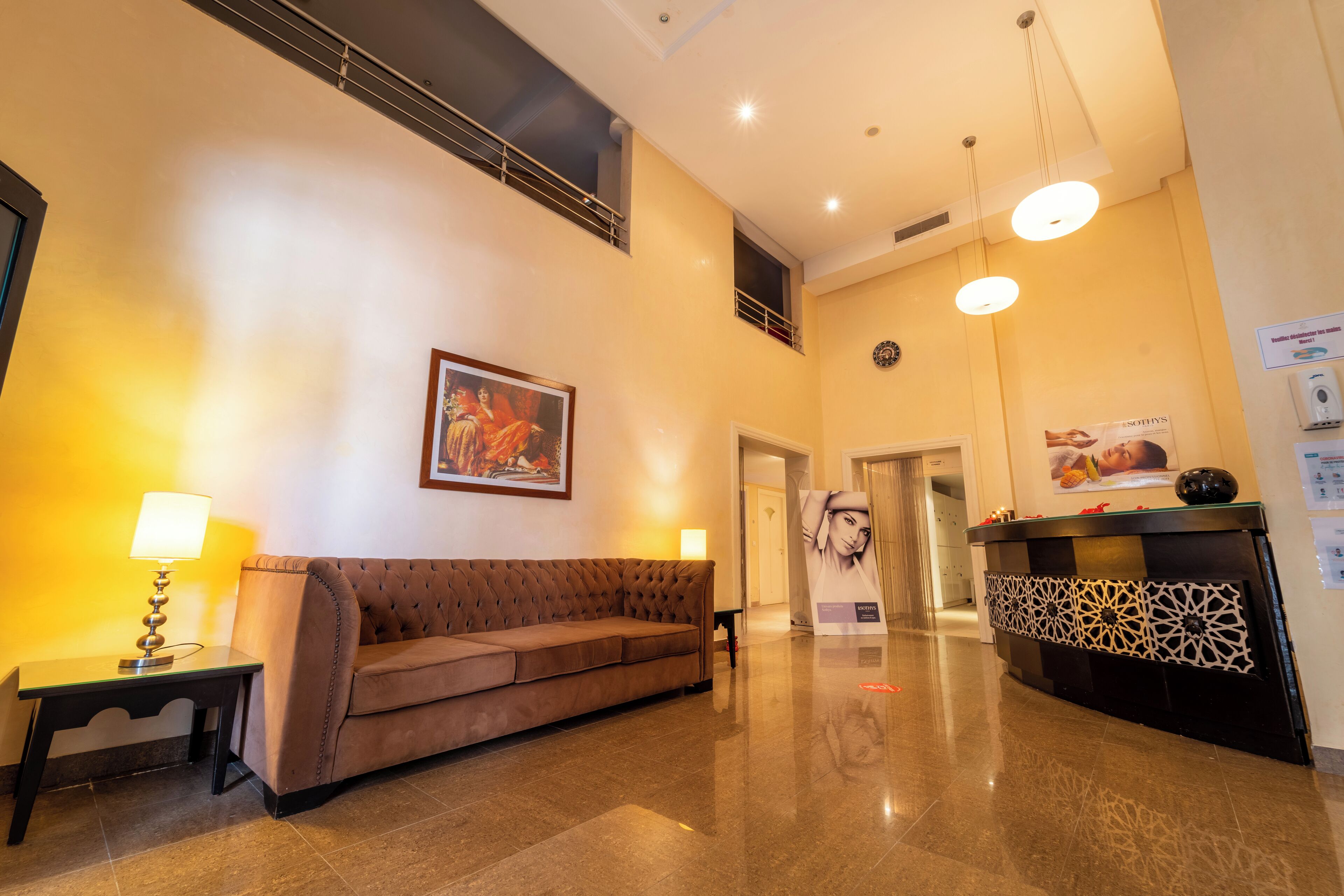 Eine Lobby mit einem braunen Sofa, einem kleinen Tisch mit Lampe, einem Empfangstresen und einem gerahmten Bild an der Wand.