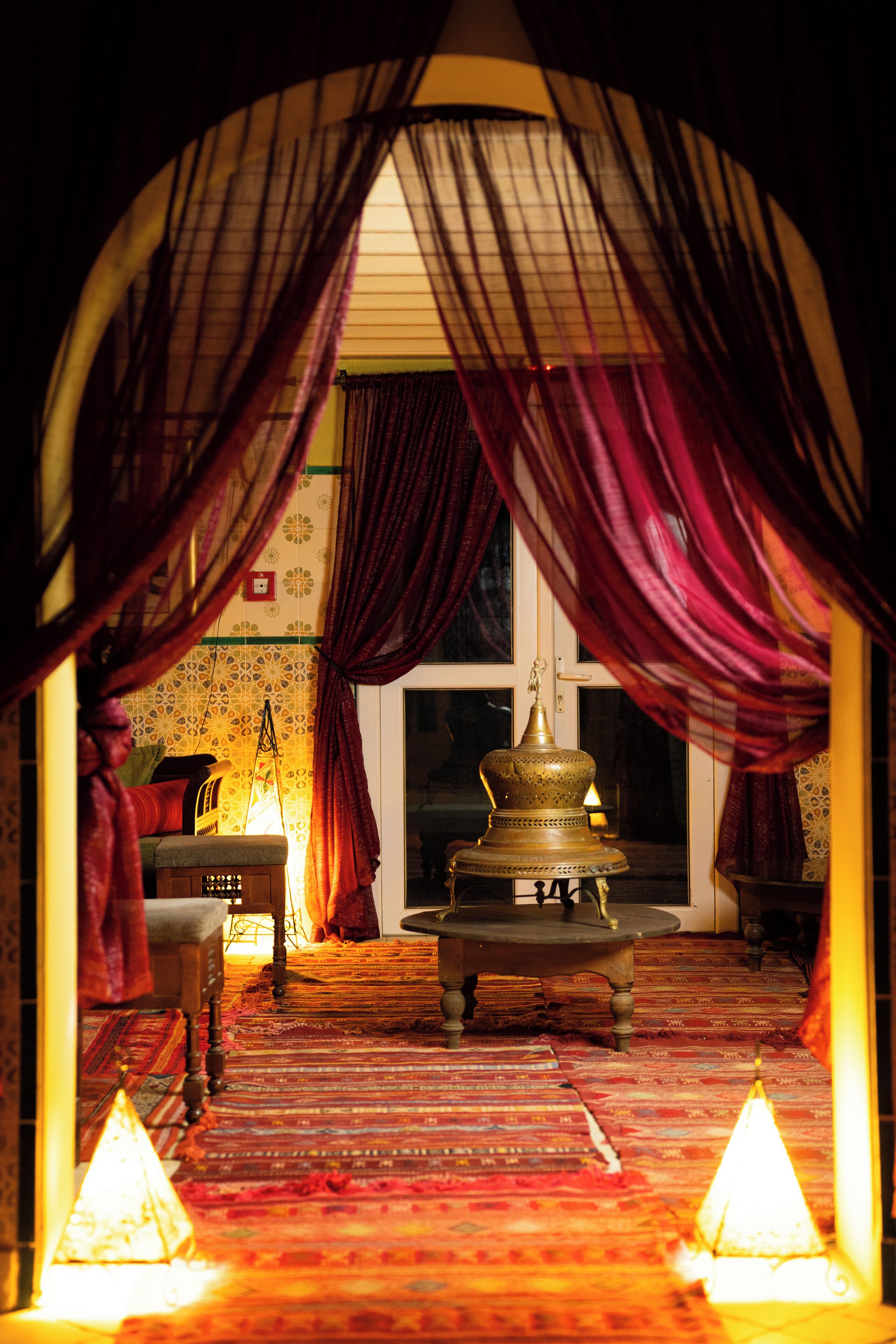 A warmly lit room with a patterned carpet, a traditional lamp, and a decorative bowl.