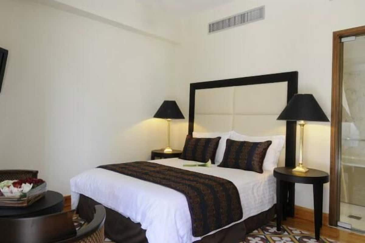 A hotel room with a large bed, two bedside tables with lamps, a small round table with a tray of flowers, and a large mirror on the wall.