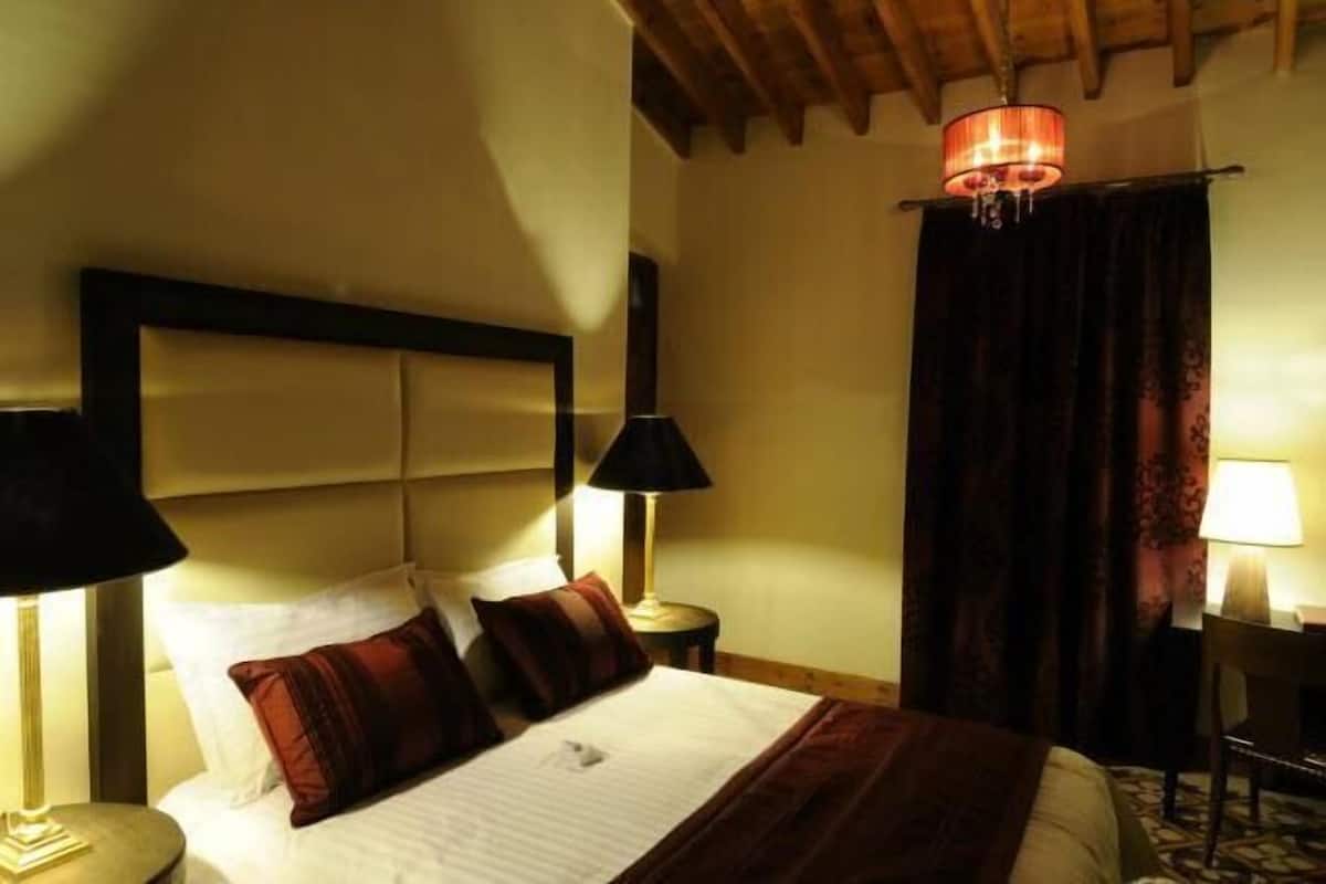 A hotel room with a large bed, two bedside lamps, a chandelier, and a desk with a chair.