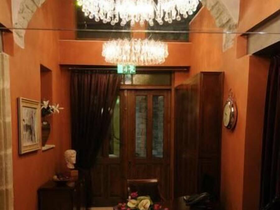 A lobby with a chandelier, wooden door, patterned rug, and a chair.