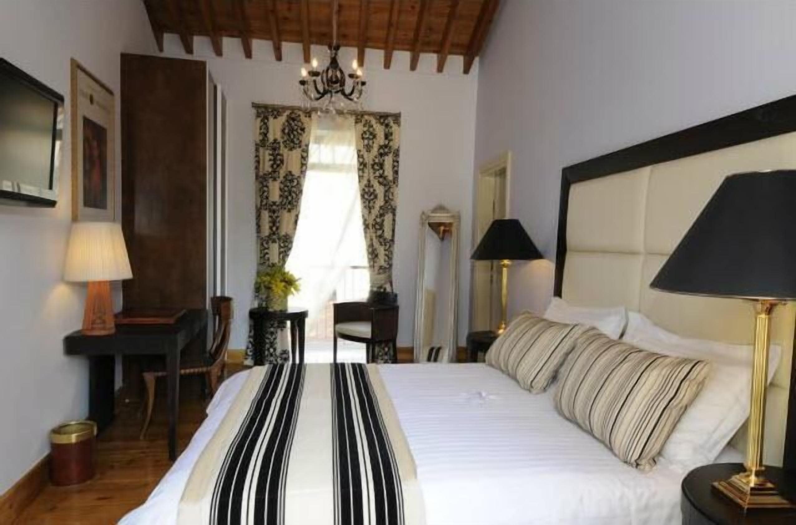 A hotel room with a large bed, a desk, a chair, a lamp, and a window with curtains.