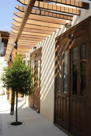 A building with a wooden pergola, large wooden doors, and a small tree in the foreground.