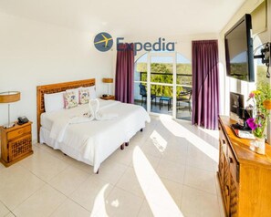 A hotel room with a bed, a desk with a computer, a TV, and a balcony with curtains.
