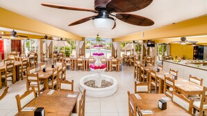 Um restaurante com várias mesas e cadeiras de madeira, uma fonte decorativa central e ventiladores de teto.