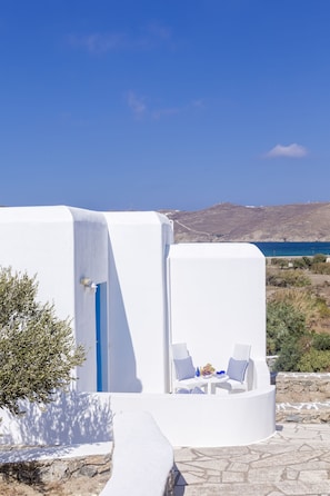 A white building with a blue door, a stone pathway, and a table with two chairs and a tablecloth. - Anamar Mykonos Natural Retreat (Mykonos)