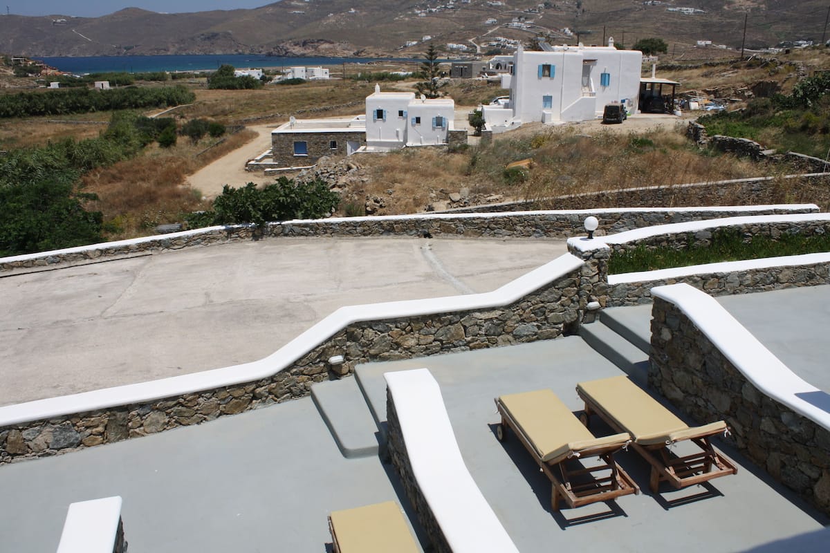 A rooftop terrace with lounge chairs and a view of white buildings and a body of water.