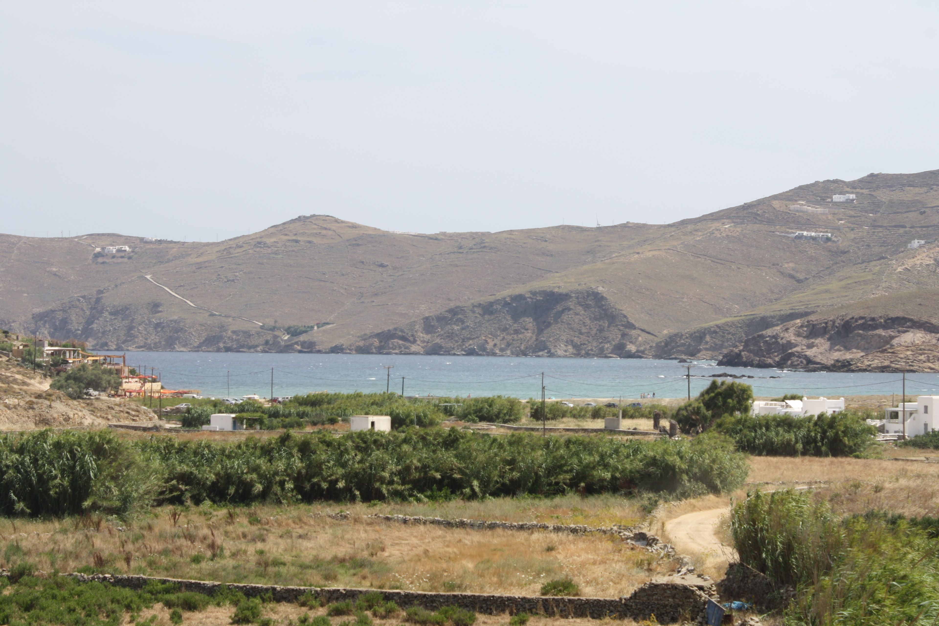 Paesaggio costiero con un sentiero sterrato che conduce a un corso d'acqua, circondato da colline e vegetazione rada.