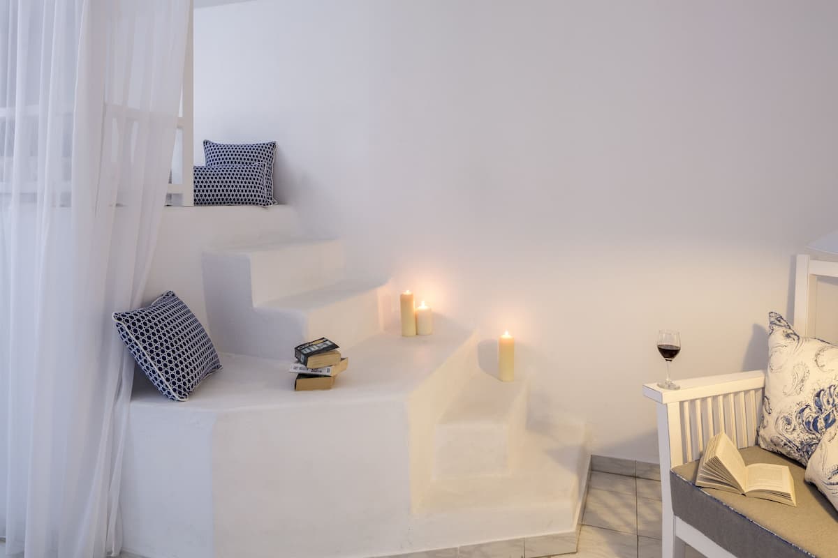 A cozy reading nook with a cushioned bench, a small table with books and candles, and a window with sheer curtains.