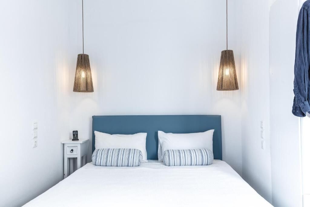 A neatly made bed with white and striped pillows, a blue headboard, and two pendant lights hanging above.