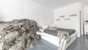 A bedroom with a bed against a white wall, a large rock feature, and three fish wall art pieces. - Anamar Mykonos Natural Retreat (Mykonos)