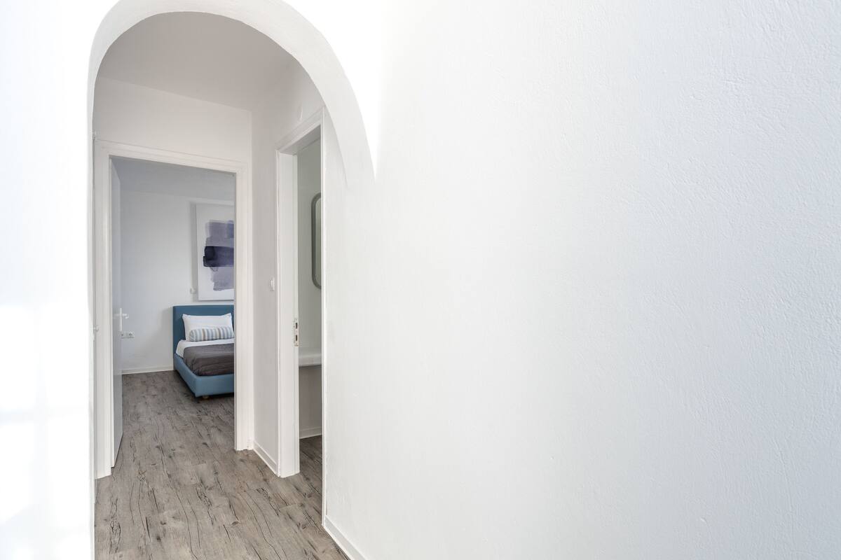 A hallway with a wooden floor leading to a bedroom with a bed and a blue headboard.