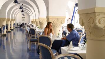 Un'area pranzo con sedie a righe blu e bianche, tavoli bianchi e pavimento piastrellato blu.