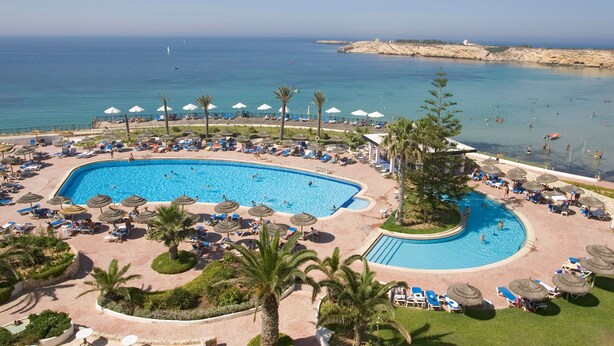 Un resort con una piscina grande, tumbonas, sombrillas y vistas al mar.