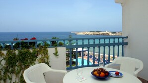 Un balcón con vista al mar, una mesa con un frutero y sillas blancas.