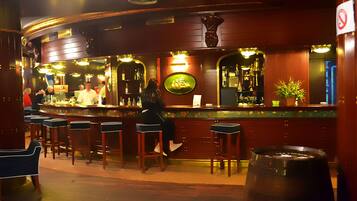 Un espace bar avec des tabourets de bar en bois, un comptoir orné d’un néon et une grande cuve à bière.
