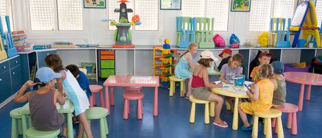 Une salle de classe où des enfants participent à des activités, avec des meubles colorés et du matériel pédagogique.