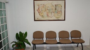 Uma área de espera com cinco cadeiras marrons e um grande quadro abstrato na parede.