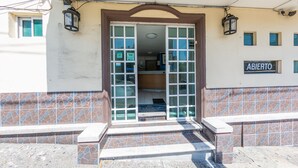 Entrada de um edifício com fachada em azulejos, uma placa com a palavra 'ABIERTO' e um conjunto de degraus que levam à porta.