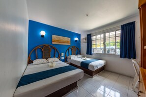 Quarto com duas camas, uma parede azul decorativa, uma janela com cortinas e uma luminária no teto.